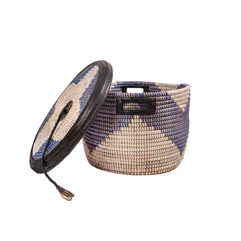 Coumba basket. A rounded woven basket with dark blue pattern on white. Black leather trim and tassel on lid. View is from the side.