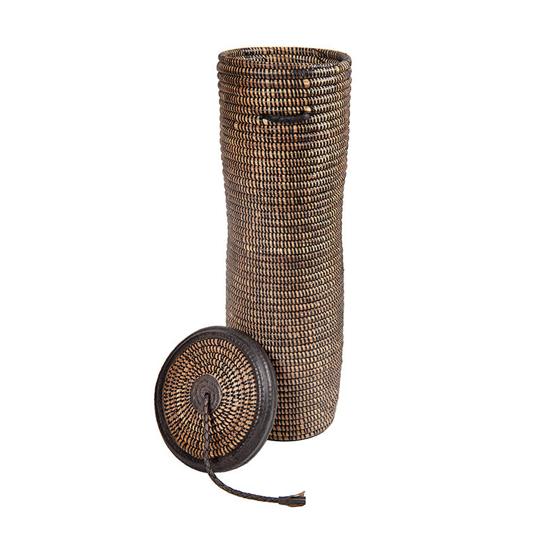 Jummy Basket on white. Tall, skinny, rounded woven basket with black details including a leather trimmed, tasseled lid.