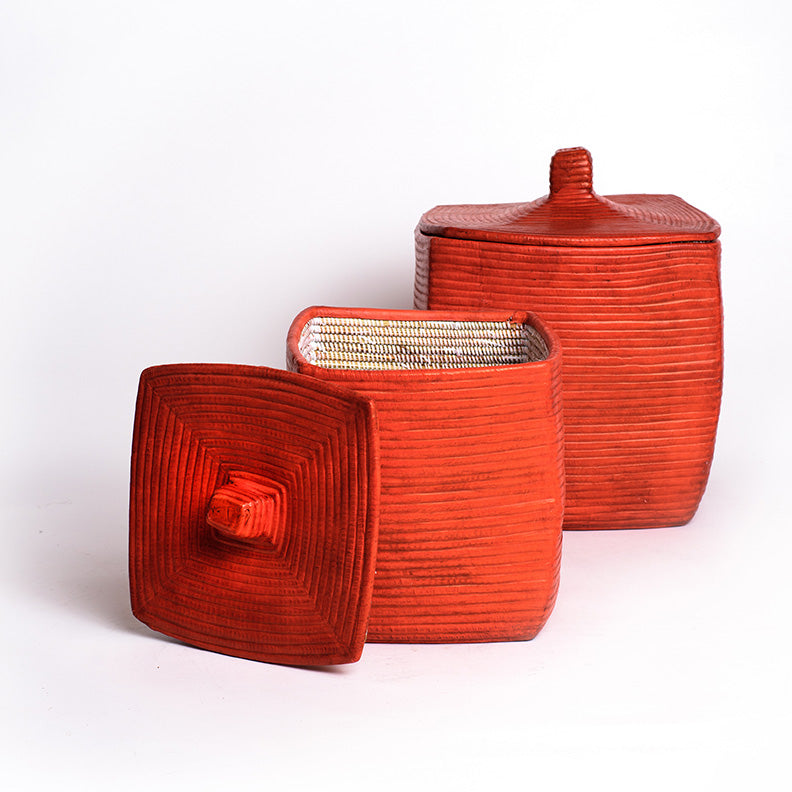 Two square woven baskets with lids and covered in red leather.